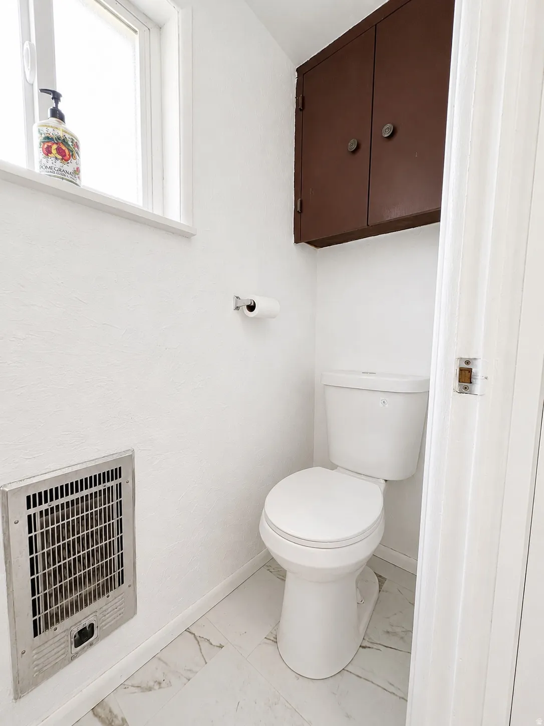 White water closet featuring a window, overhead cabinetry, wall-mounted register, and white tile flooring