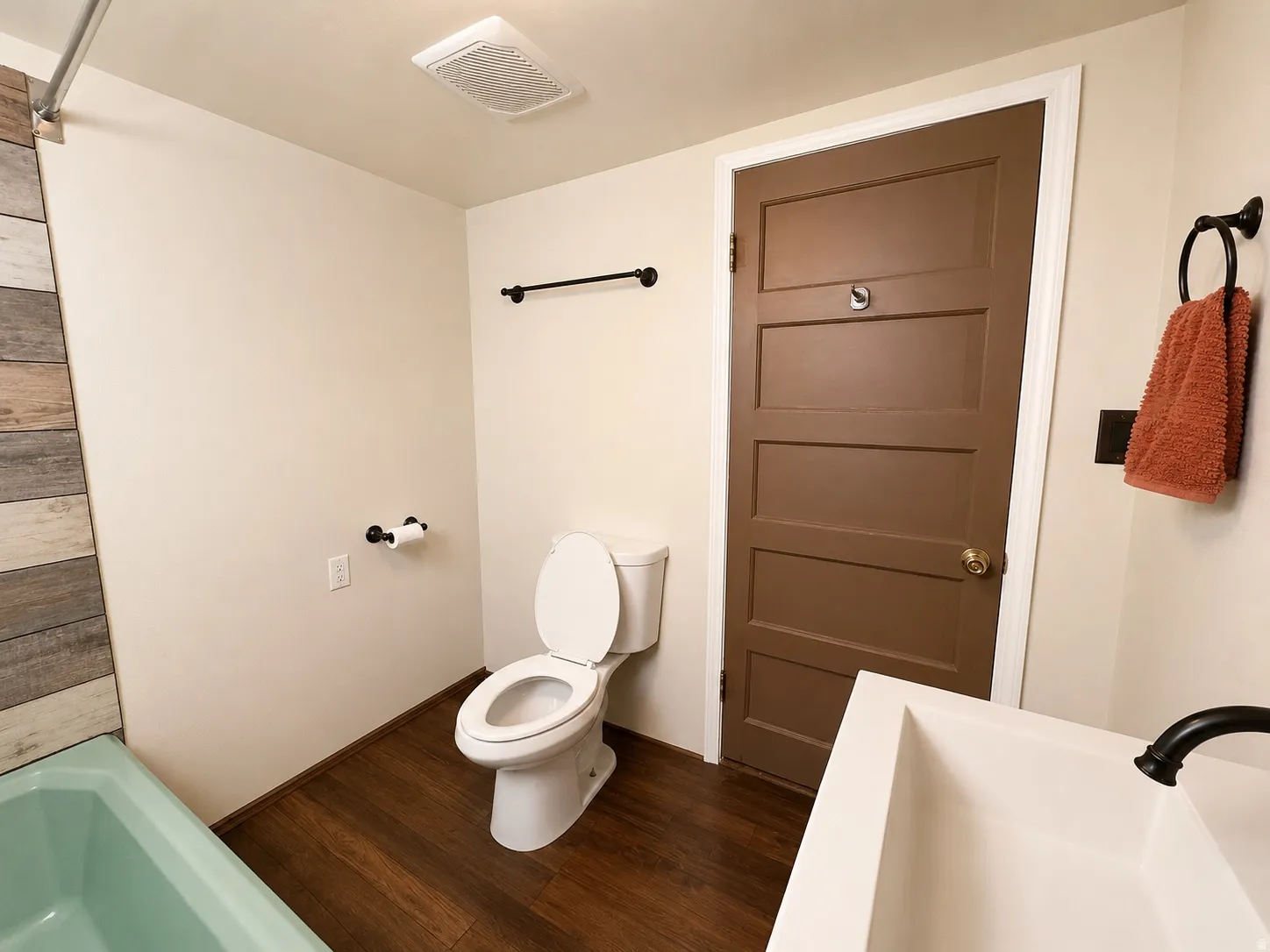Bathroom featuring wood-finish flooring, a white toilet, and a mint green bathtub