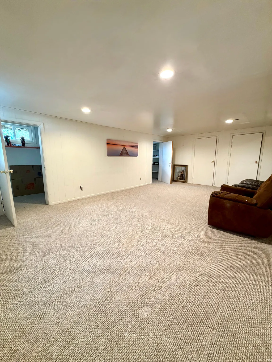 Expansive carpeted room featuring recessed lighting, multiple closed doors, and a partial egress window