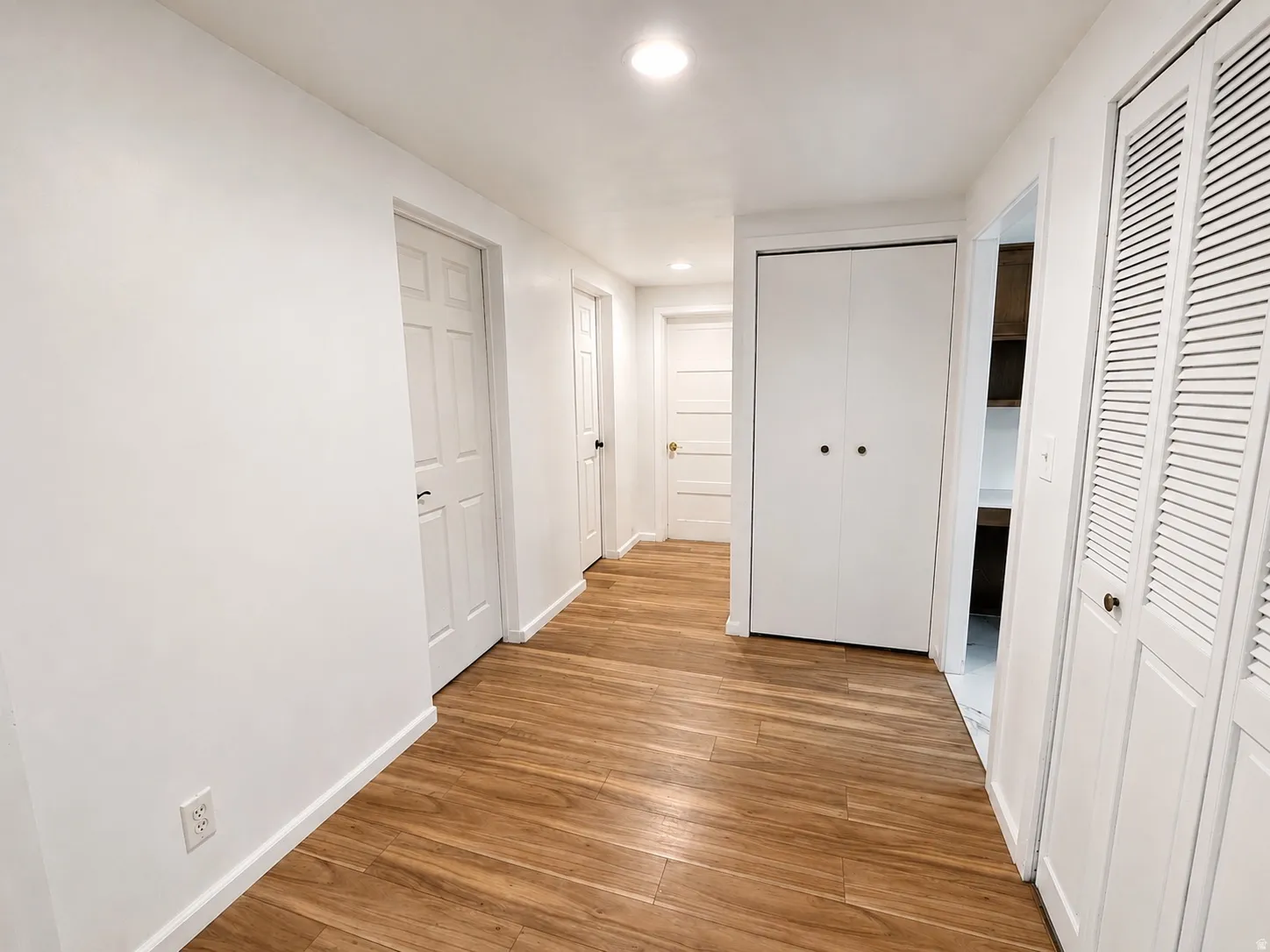Hallway featuring wood-finish flooring, white walls, multiple paneled doors, and bi-fold louvered closet doors