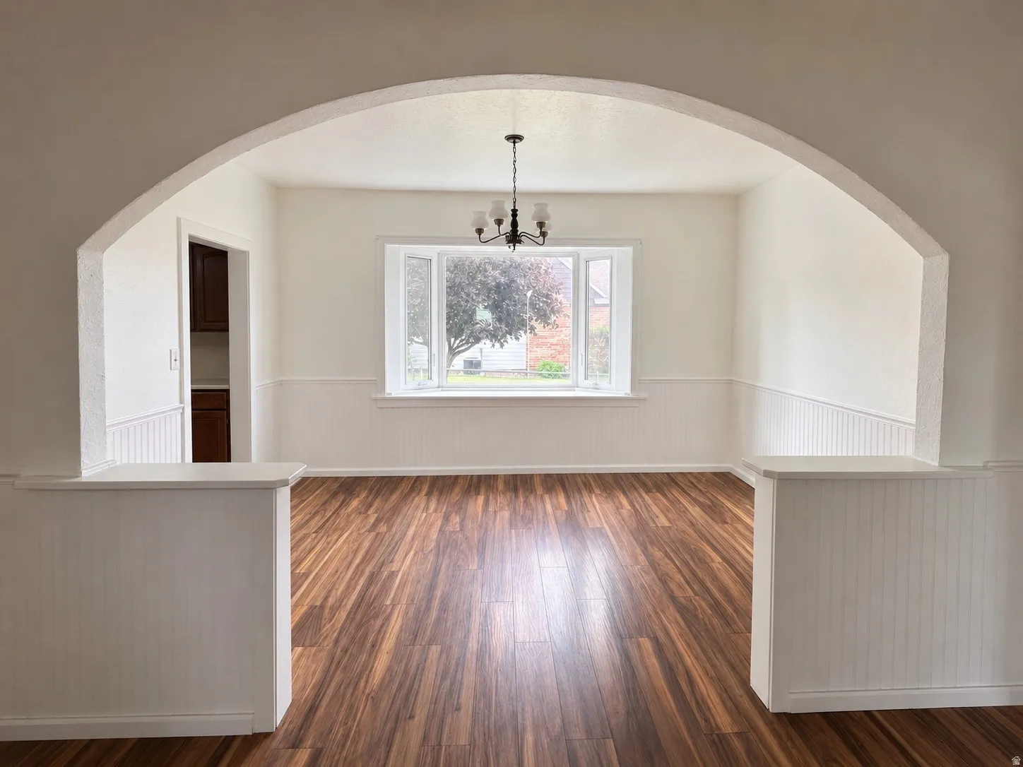 Spacious room featuring wood-finish flooring, wainscoting, and an arched entryway