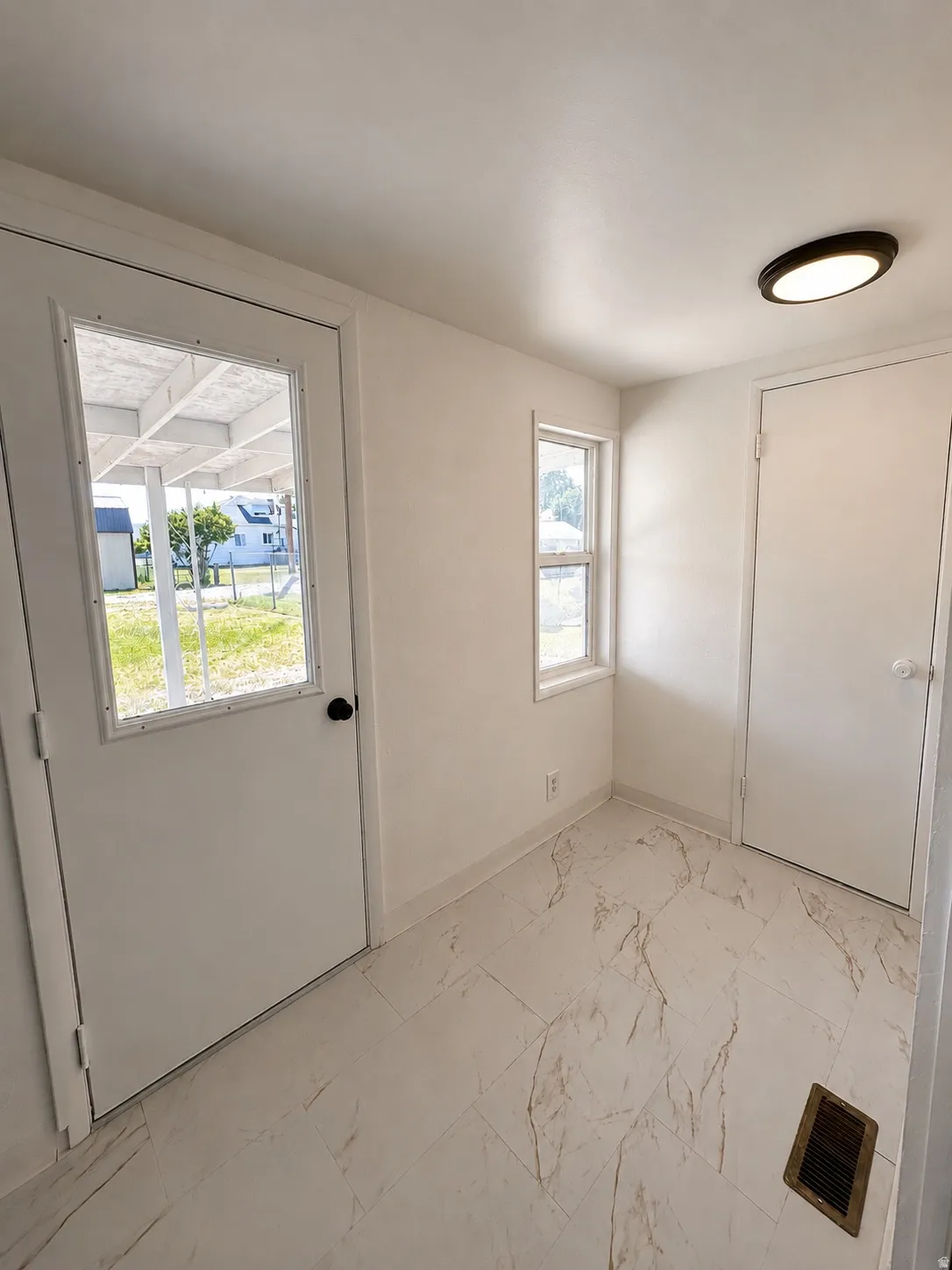 Entryway featuring light-toned tile flooring with subtle veining, white walls, and a ceiling-mounted flush light fixture