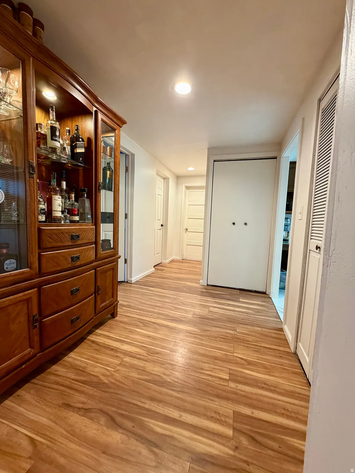 Hallway featuring wood-finish flooring, recessed lighting, white interior doors, and a built-in cabinetry unit with glass display panels