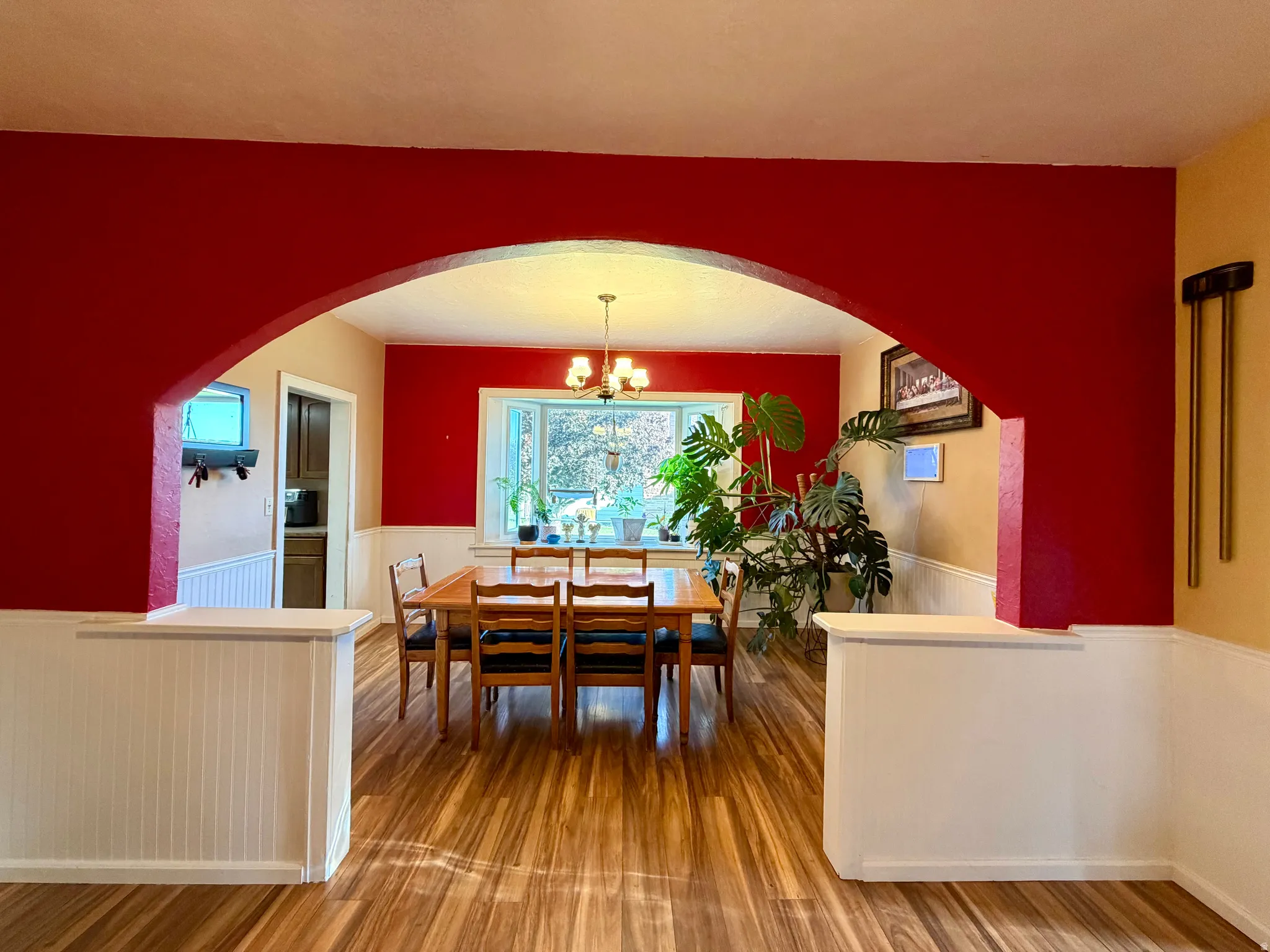 Dining area featuring an arched entryway, bay window, wood-finish flooring, and wainscoting