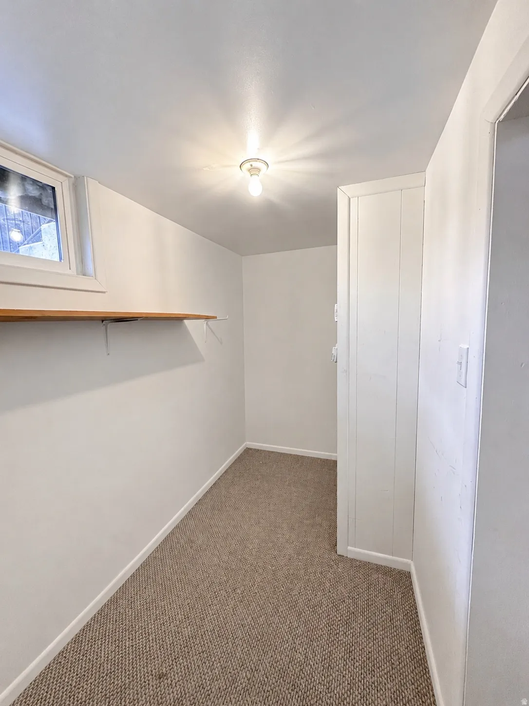Carpeted room featuring a single window, overhead flush-mount lighting, and a built-in wall shelf