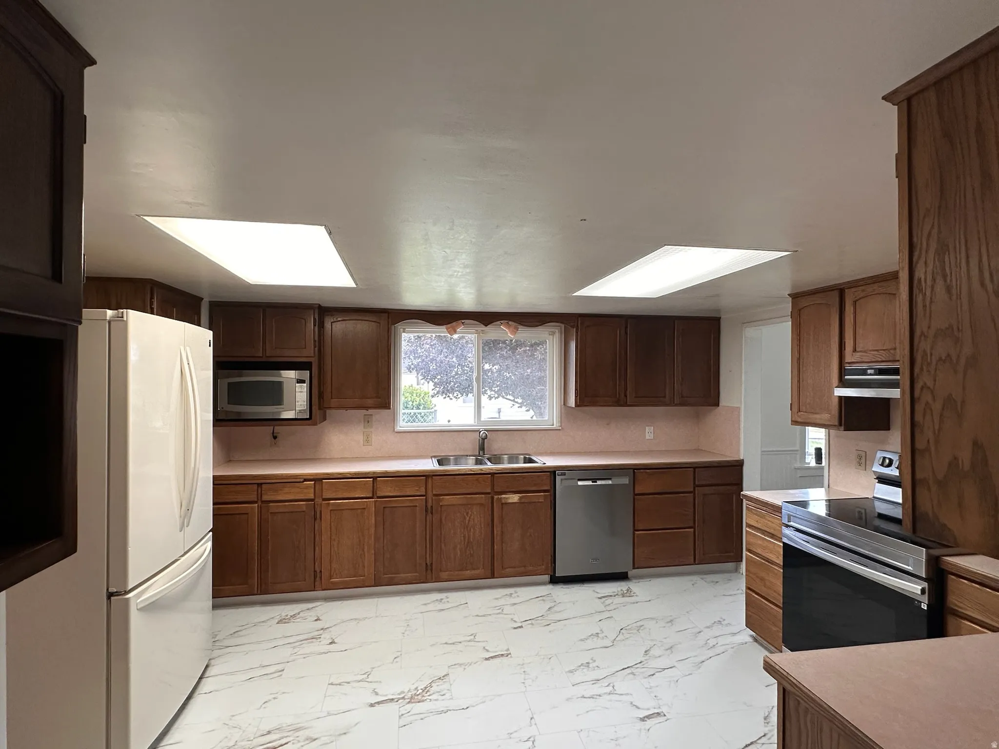 Kitchen featuring wood cabinetry, white tile flooring, stainless steel dishwasher, and two skylights
