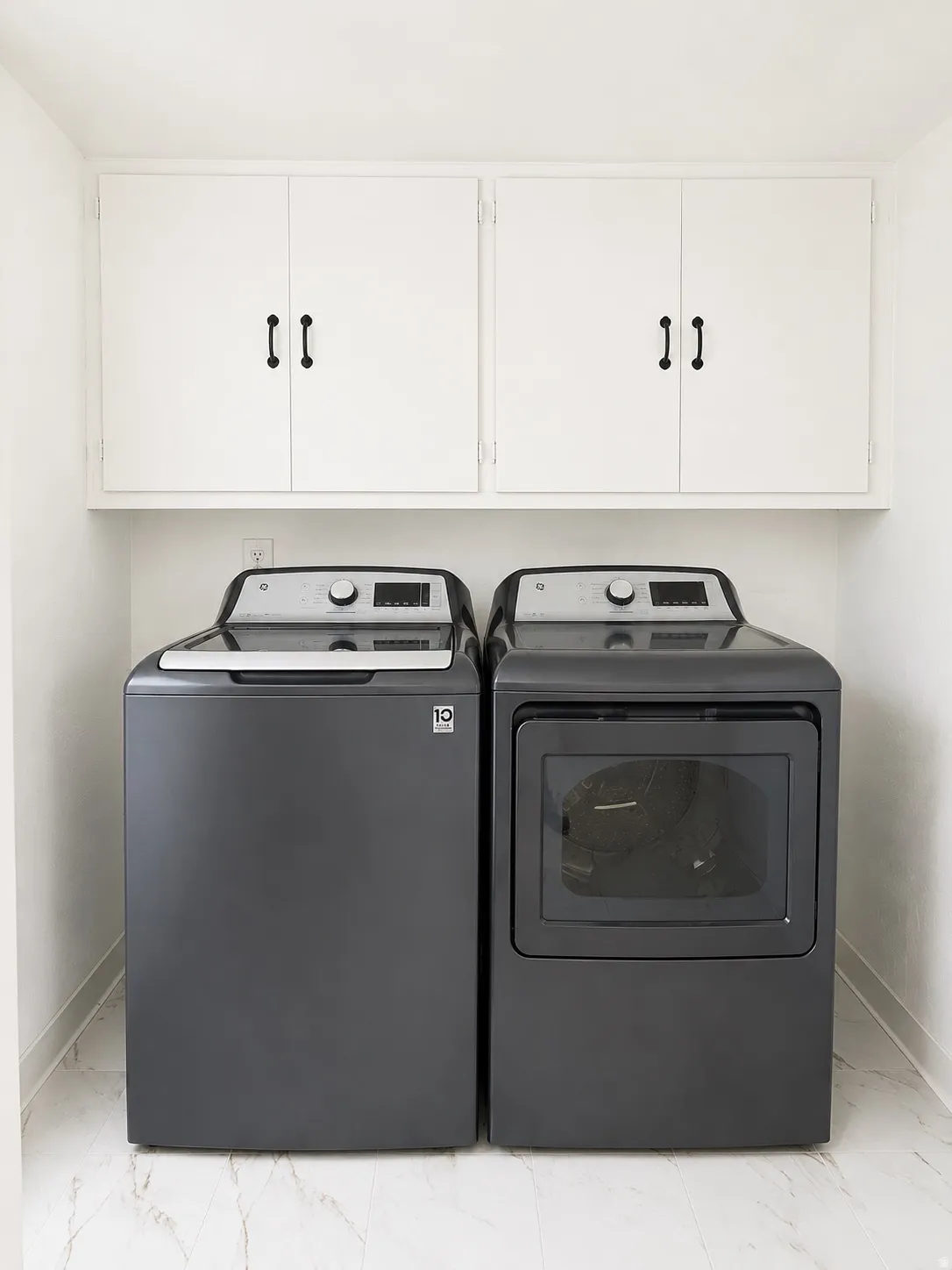 Dedicated laundry area featuring white upper cabinetry with dark hardware and light-toned, veined flooring