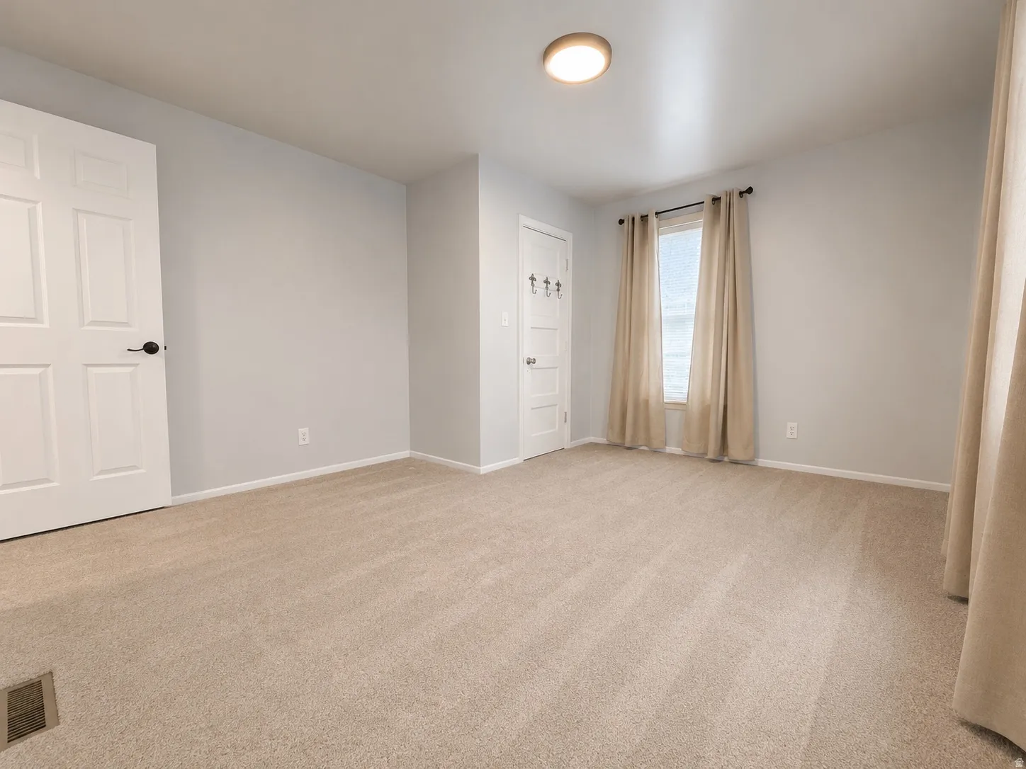 Spacious room with light neutral carpet flooring, light gray wall paint, and white trim