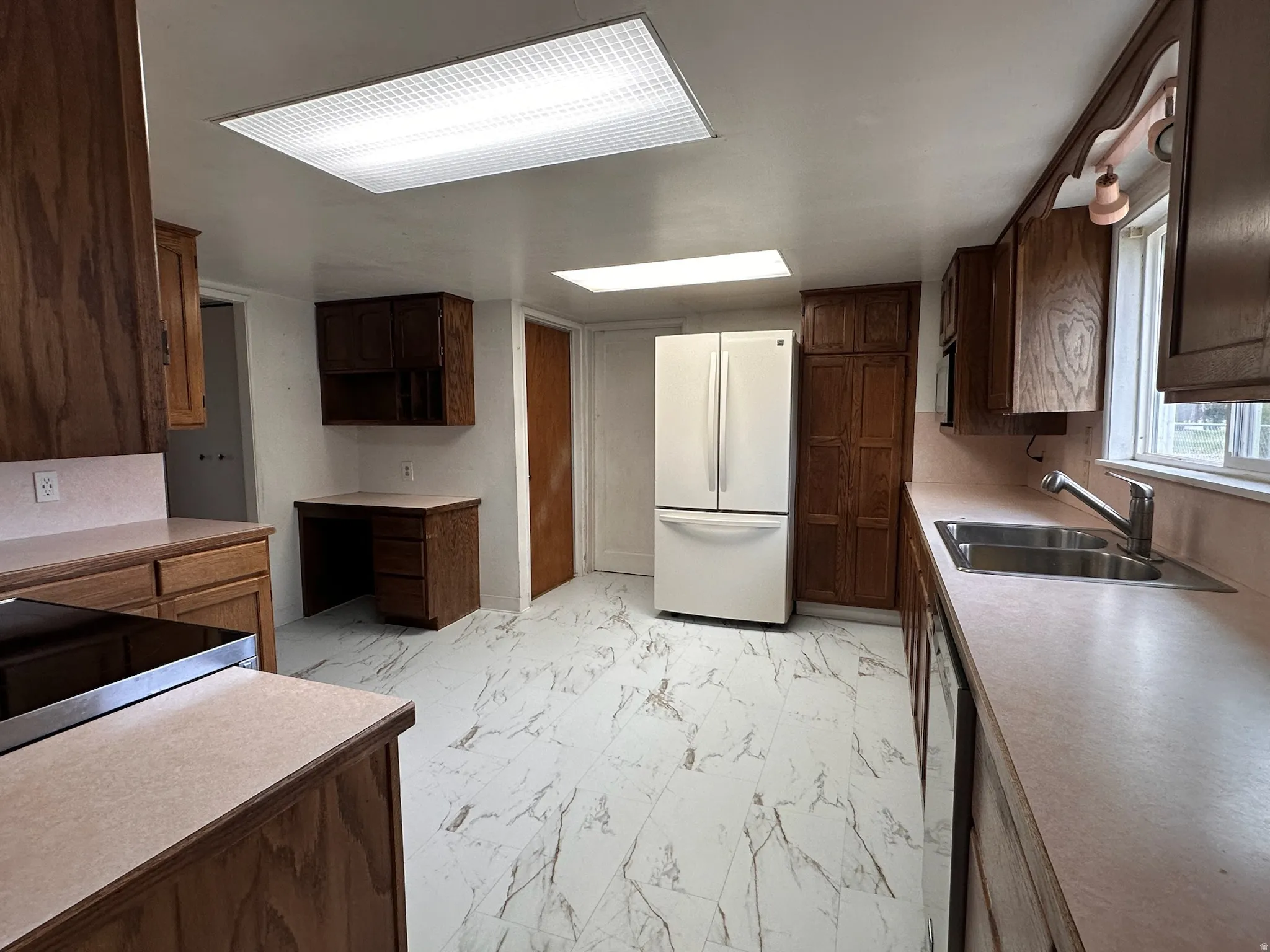 Spacious kitchen featuring wood cabinetry, light-toned countertops, and a double-basin stainless steel sink