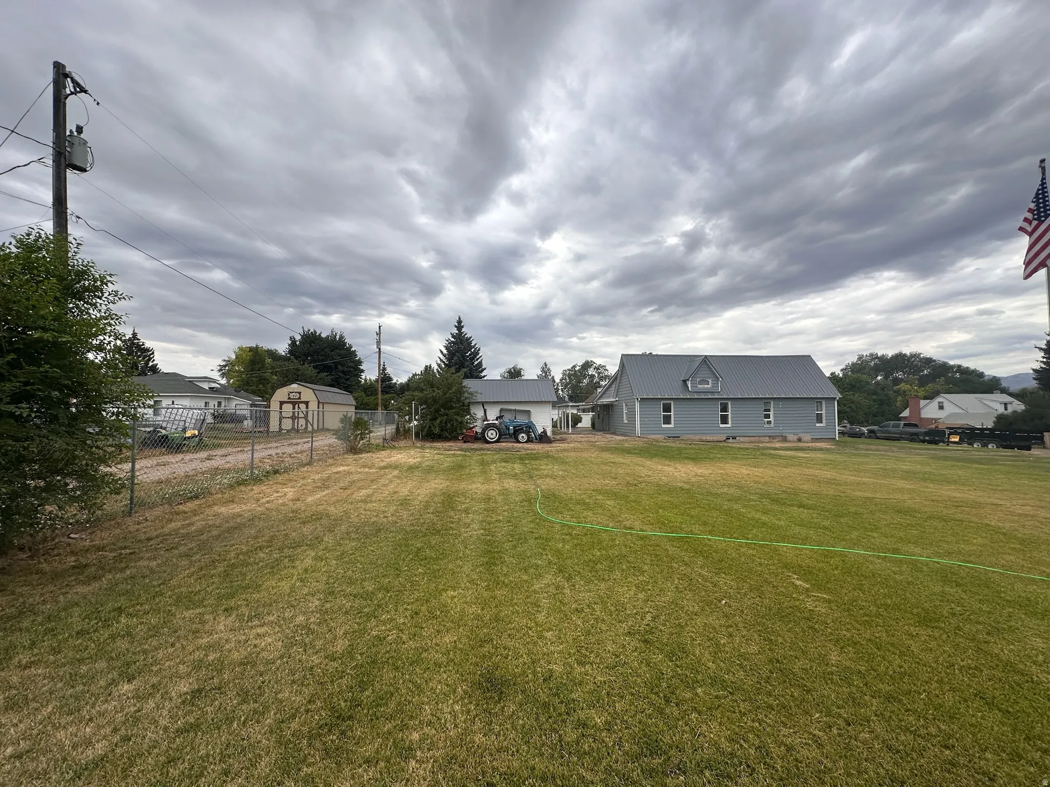 Expansive green lawn with a chain-link fence bordering a gravel driveway