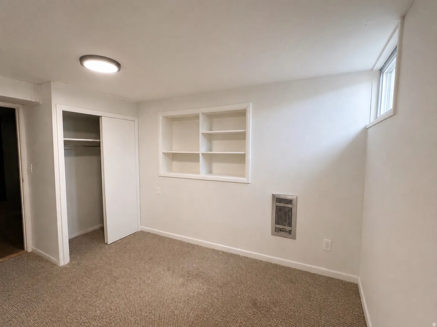 Carpeted interior space featuring white walls and a built-in shelving unit