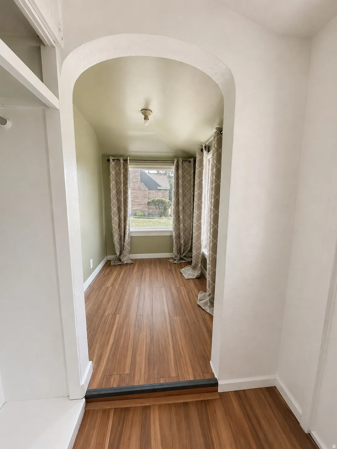 Archway entry opening to a room featuring wood-finish flooring, light green wall paint, and a window with trim