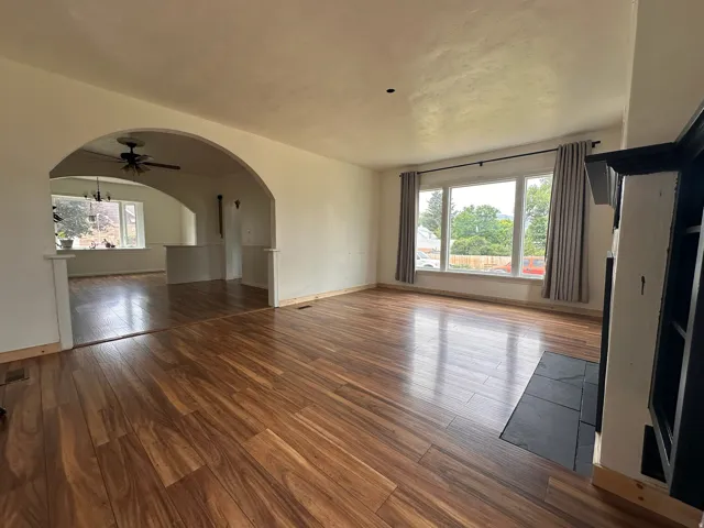 Spacious interior featuring wood-finish flooring, a prominent arched doorway, and a fireplace with a dark-tiled hearth and built-in shelving