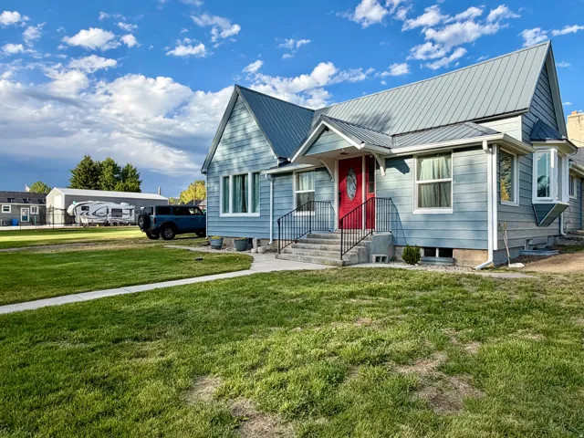 Light blue siding exterior featuring a red entry door, a prominent bay window, and a gray metal roof