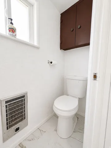 White water closet featuring a window, overhead cabinetry, wall-mounted register, and white tile flooring