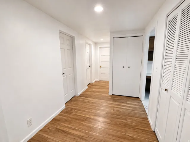 Hallway featuring wood-finish flooring, white walls, multiple paneled doors, and bi-fold louvered closet doors