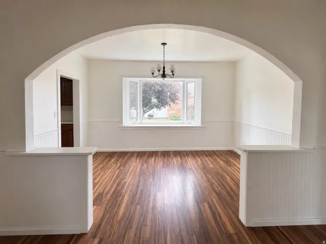 Spacious room featuring wood-finish flooring, wainscoting, and an arched entryway