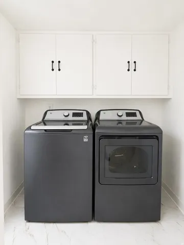 Dedicated laundry area featuring white upper cabinetry with dark hardware and light-toned, veined flooring