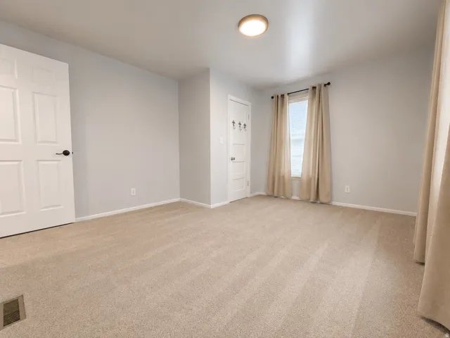 Spacious room with light neutral carpet flooring, light gray wall paint, and white trim