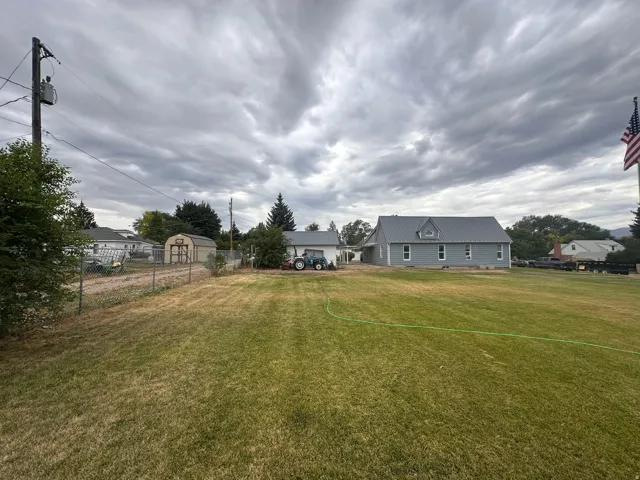 Expansive green lawn with a chain-link fence bordering a gravel driveway