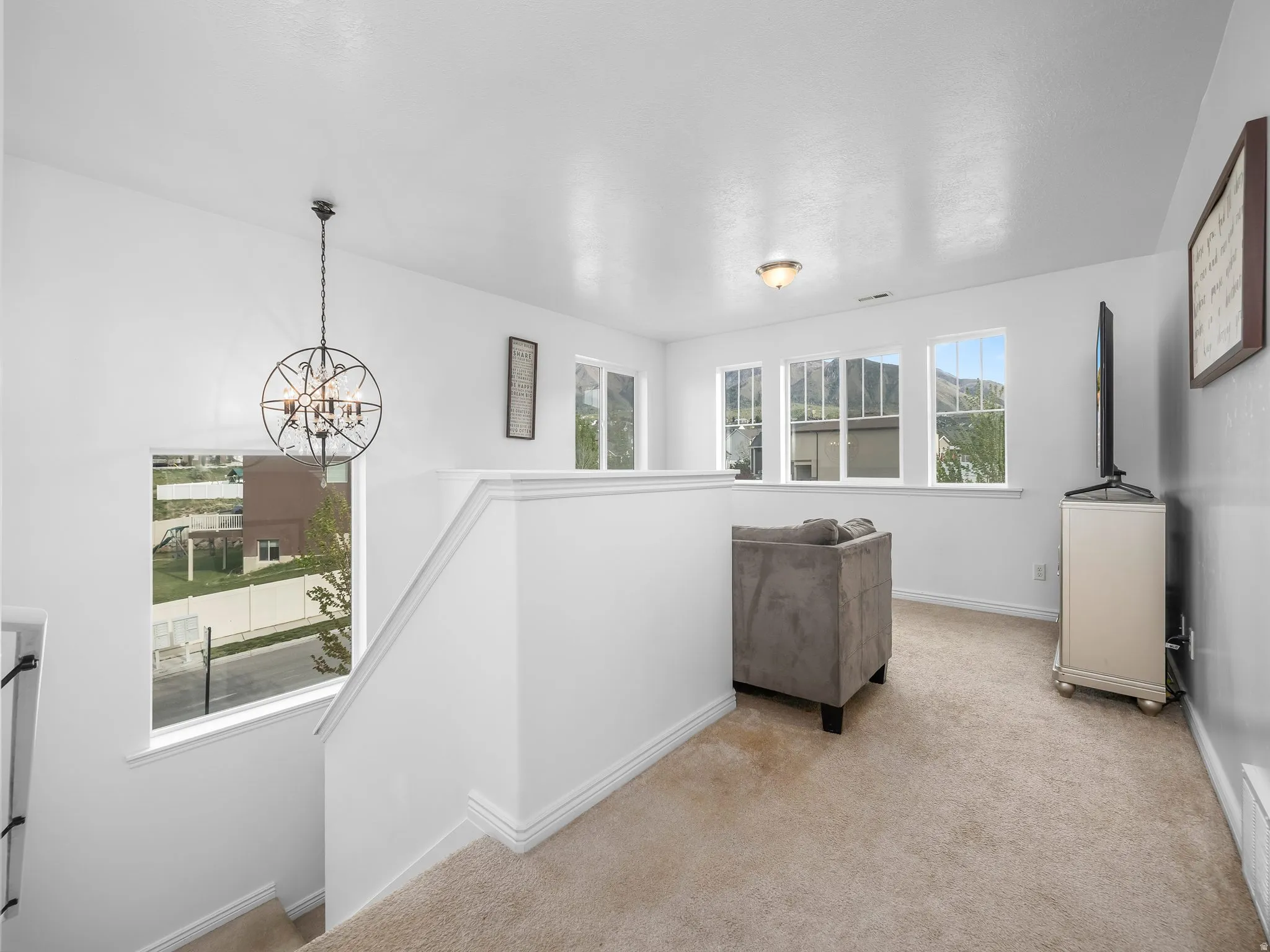 Hallway featuring light carpet, a chandelier, and an upstairs landing