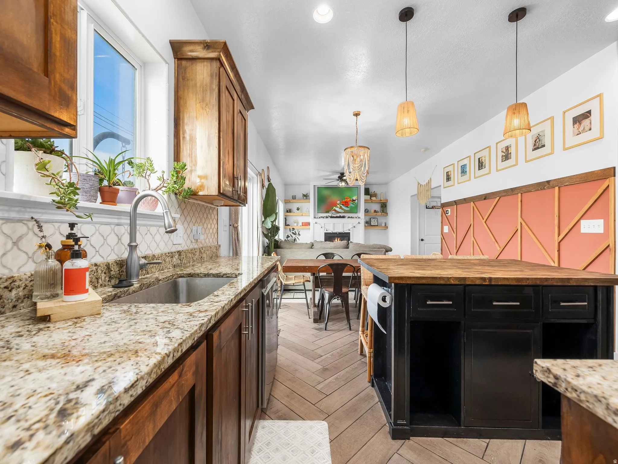 Kitchen featuring pendant lighting, light stone counters, a warm lit fireplace, light wood-style flooring, and dark cabinetry