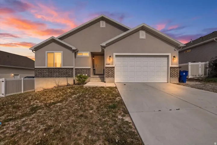 View of front of home featuring an attached garage, stucco siding, driveway, brick siding, and a gate