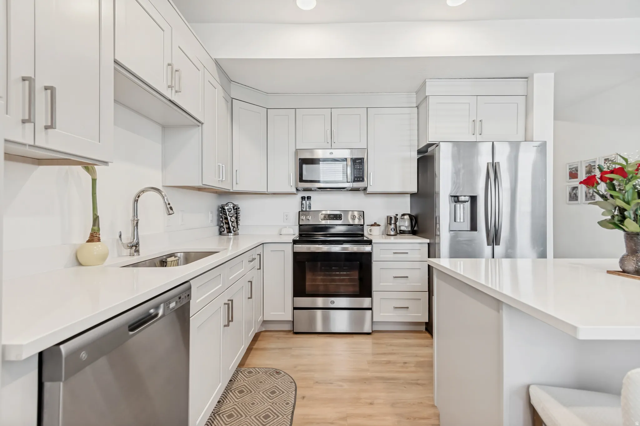 Kitchen featuring stainless steel appliances, light wood-style flooring, light stone counters, and white cabinetry