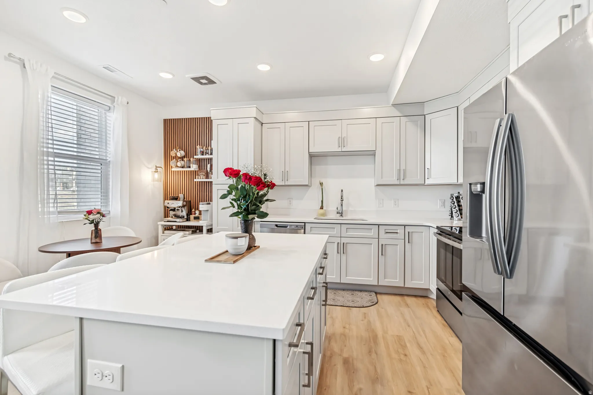 Kitchen with stainless steel appliances, light wood-style floors, recessed lighting, a center island, and light stone counters