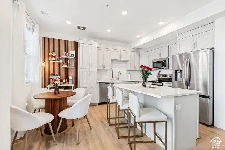 Kitchen with stainless steel appliances, a kitchen island, light wood-style floors, a kitchen breakfast bar, and recessed lighting