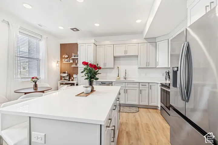Kitchen with stainless steel appliances, light wood-style floors, recessed lighting, a center island, and light stone counters