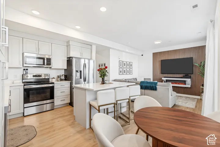 Kitchen with stainless steel appliances, open floor plan, light wood-style floors, a breakfast bar, and a kitchen island