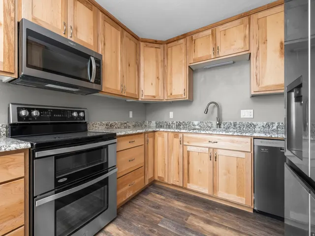 Kitchen with stainless steel appliances, light stone countertops, light wood finish cabinetry, and dark wood finished floors