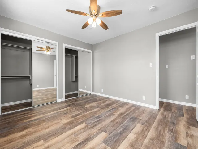 Unfurnished bedroom featuring two closets, a ceiling fan, and dark wood-type flooring