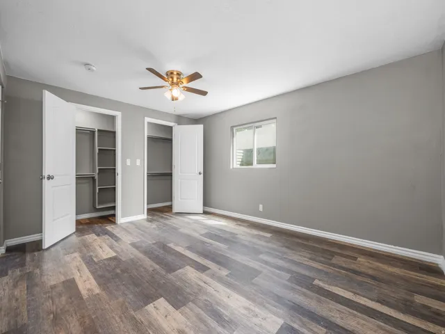 Unfurnished bedroom with multiple closets, a ceiling fan, and dark wood-style floors