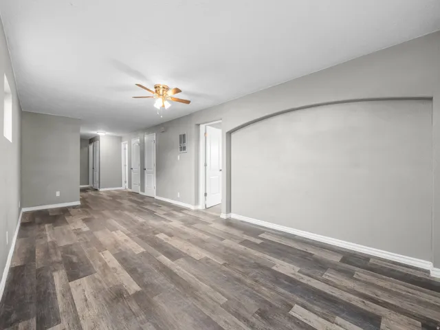 Unfurnished living room featuring a ceiling fan and dark wood-style floors