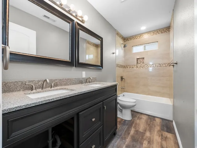 Bathroom with double vanity, shower / tub combination, and dark wood-style flooring