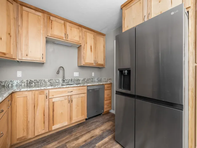 Kitchen with light wood finish cabinetry, stainless steel appliances, light stone counters, and dark wood-style flooring