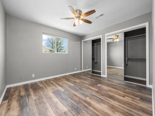 Unfurnished bedroom with multiple closets, a ceiling fan, and dark wood-type flooring