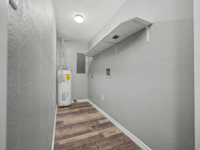 Laundry room featuring a textured wall, dark wood-style flooring, hookup for a washing machine, electric water heater, and electric panel