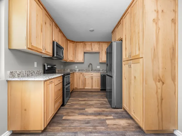 Kitchen featuring light wood finish cabinetry, stainless steel appliances, dark wood finished floors, and light stone counters