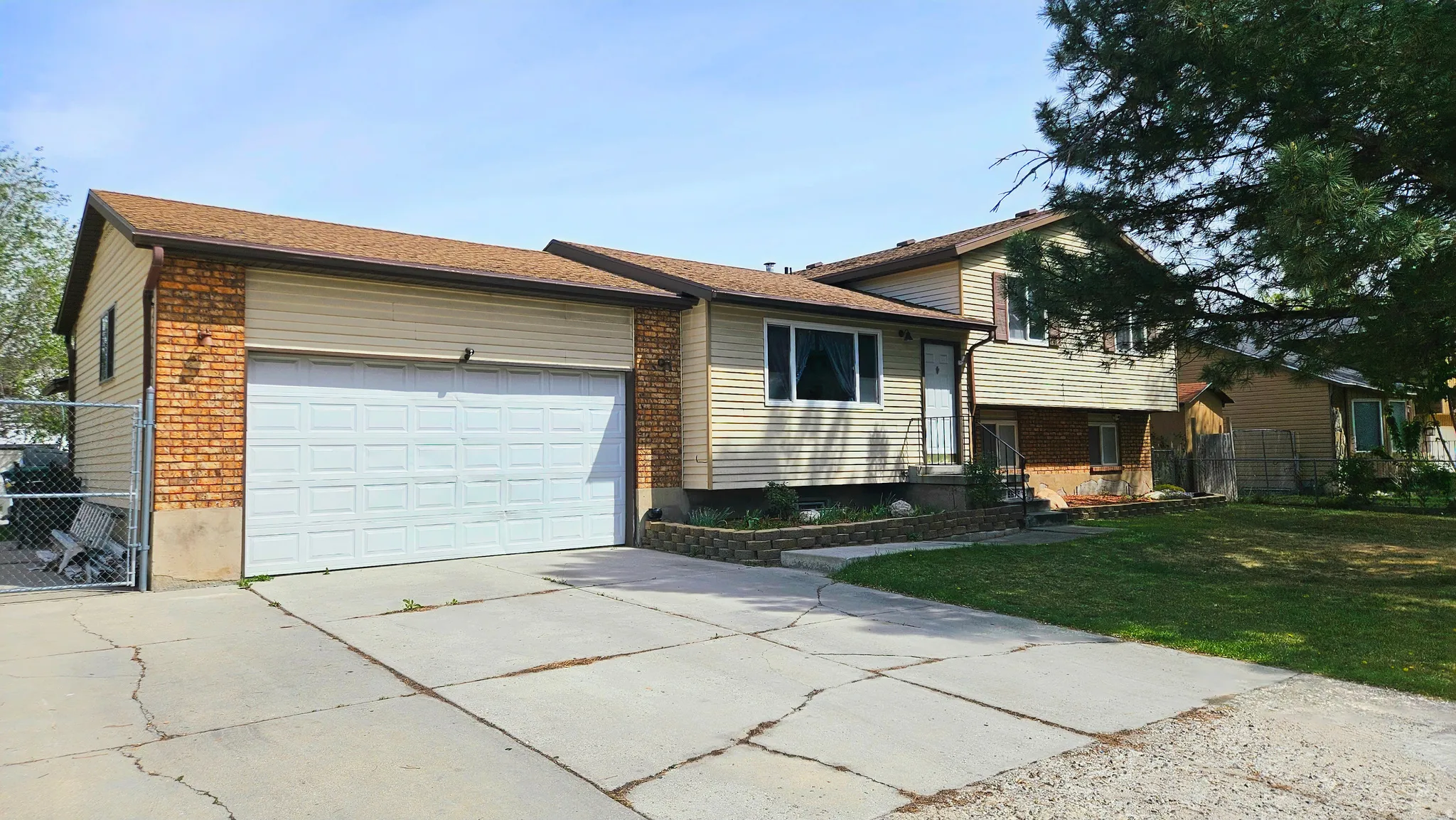 Split level home with concrete driveway, a garage, brick siding, and a gate