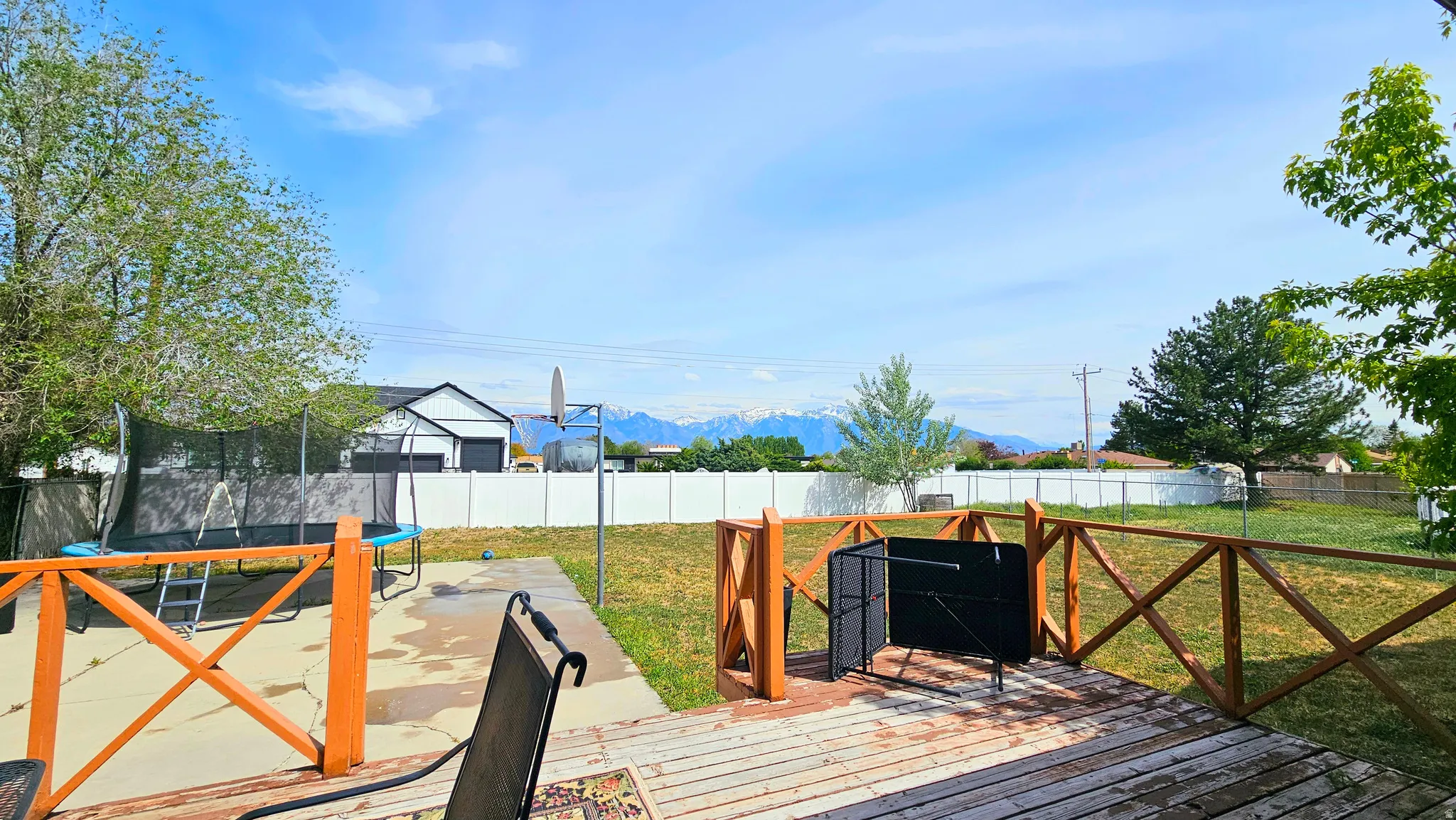 Wooden terrace with a trampoline, a fenced backyard, and a mountain view