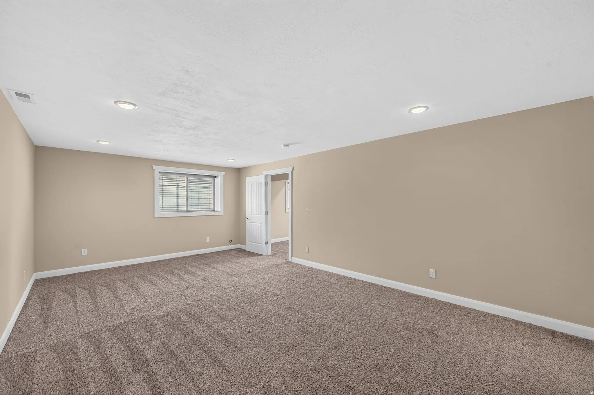 Spacious room featuring neutral-toned walls, recessed lighting, and soft pile carpet flooring