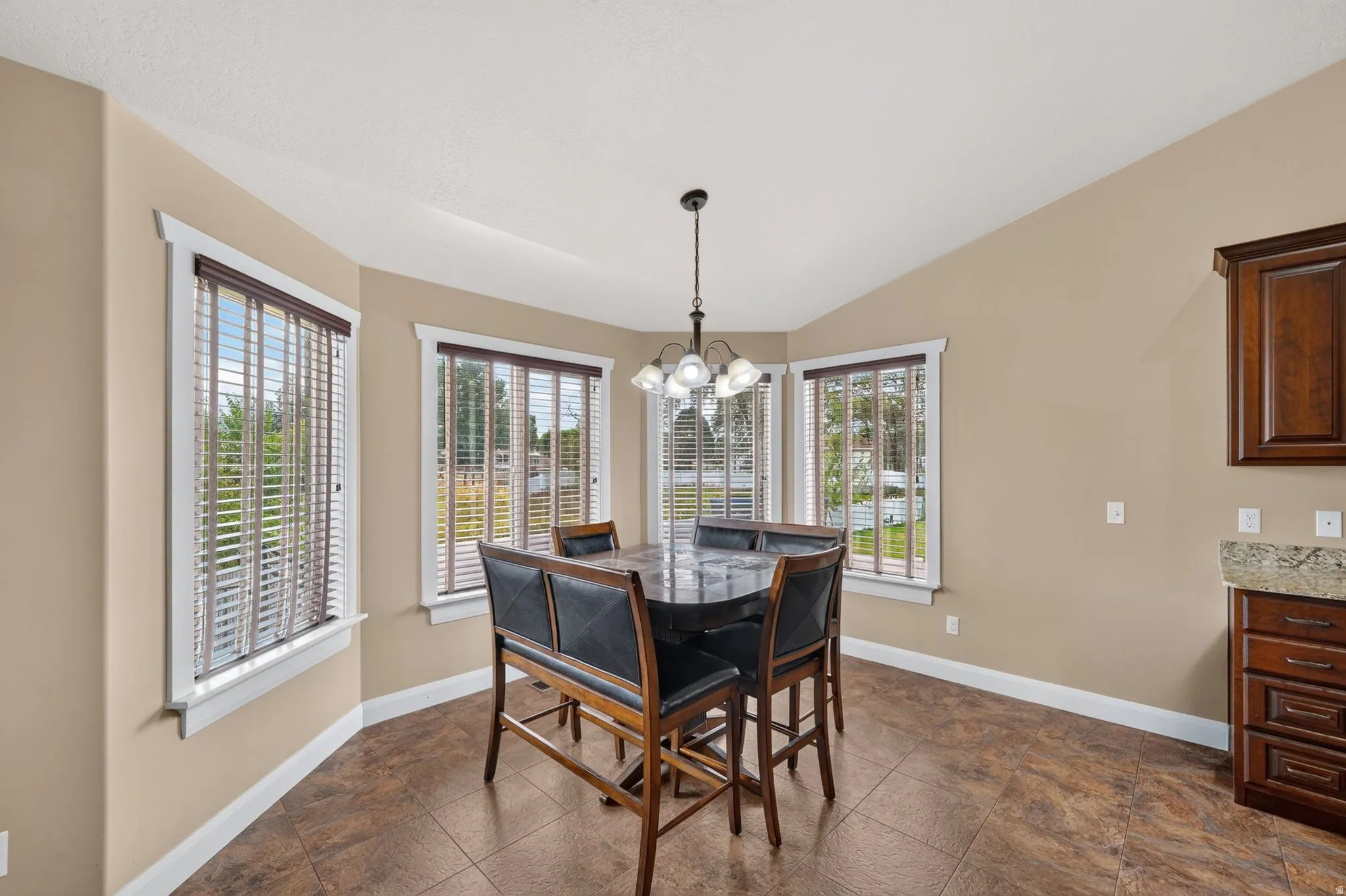 Breakfast nook featuring bay windows with blinds, a vaulted ceiling, a hanging chandelier, and tile flooring