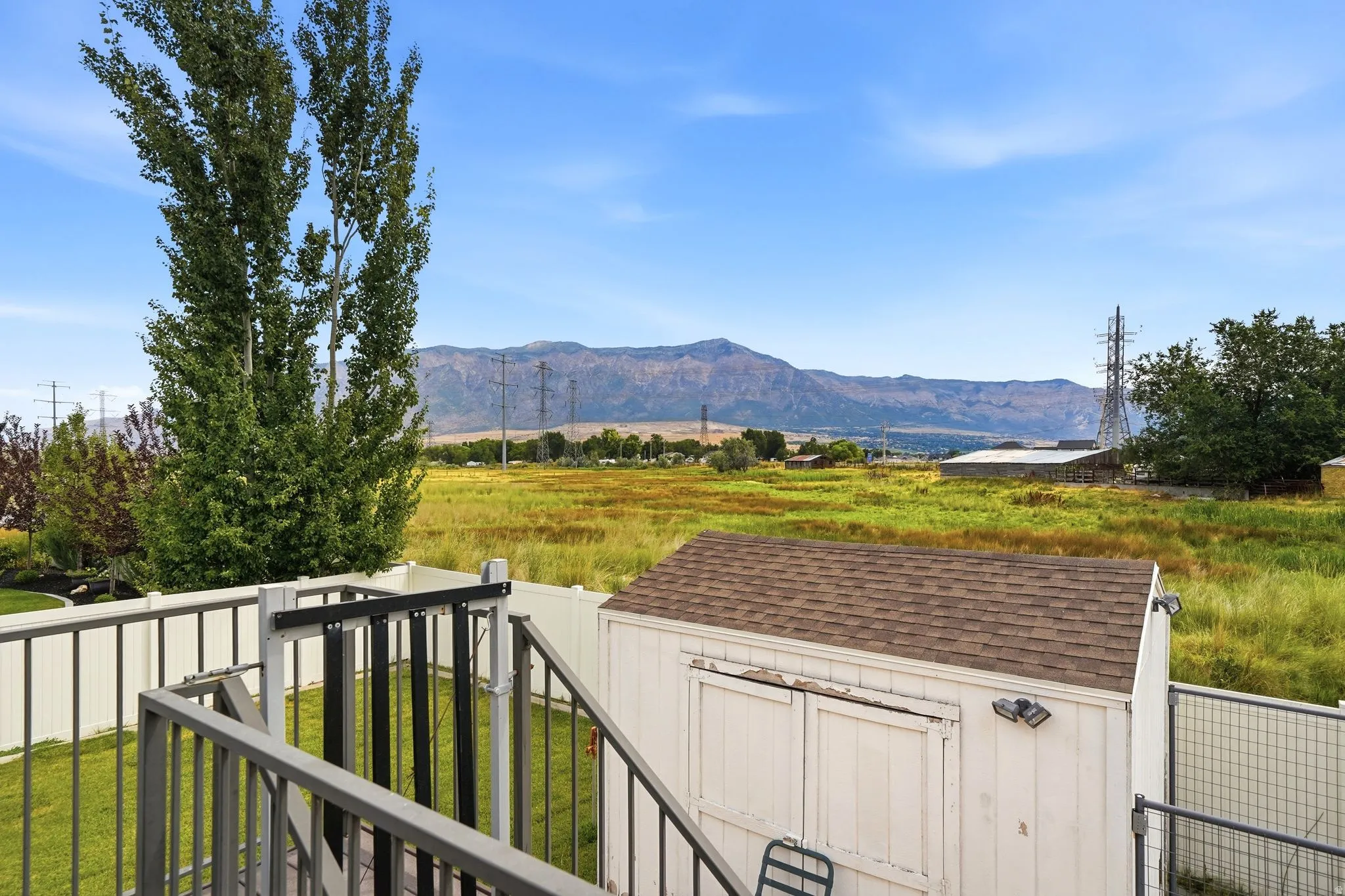 Expansive outdoor setting featuring a storage shed with shingle roofing, a manicured lawn area, and a white privacy fence