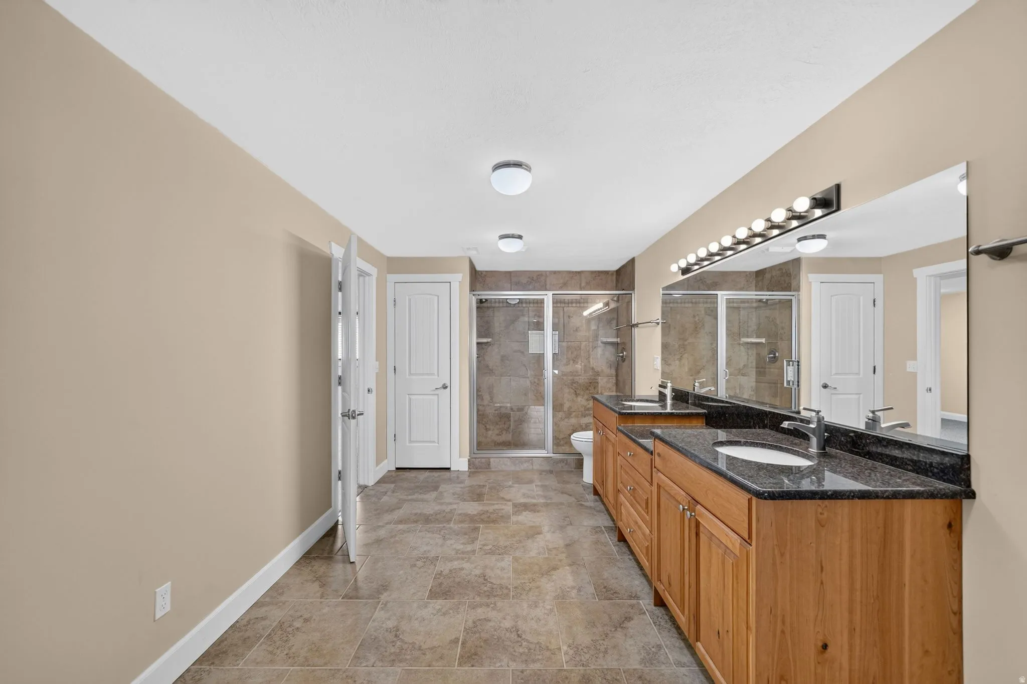 Spacious bathroom featuring dual wood vanities with dark countertops, two large mirrors with vanity lighting, and multiple enclosed showers with tiled surrounds