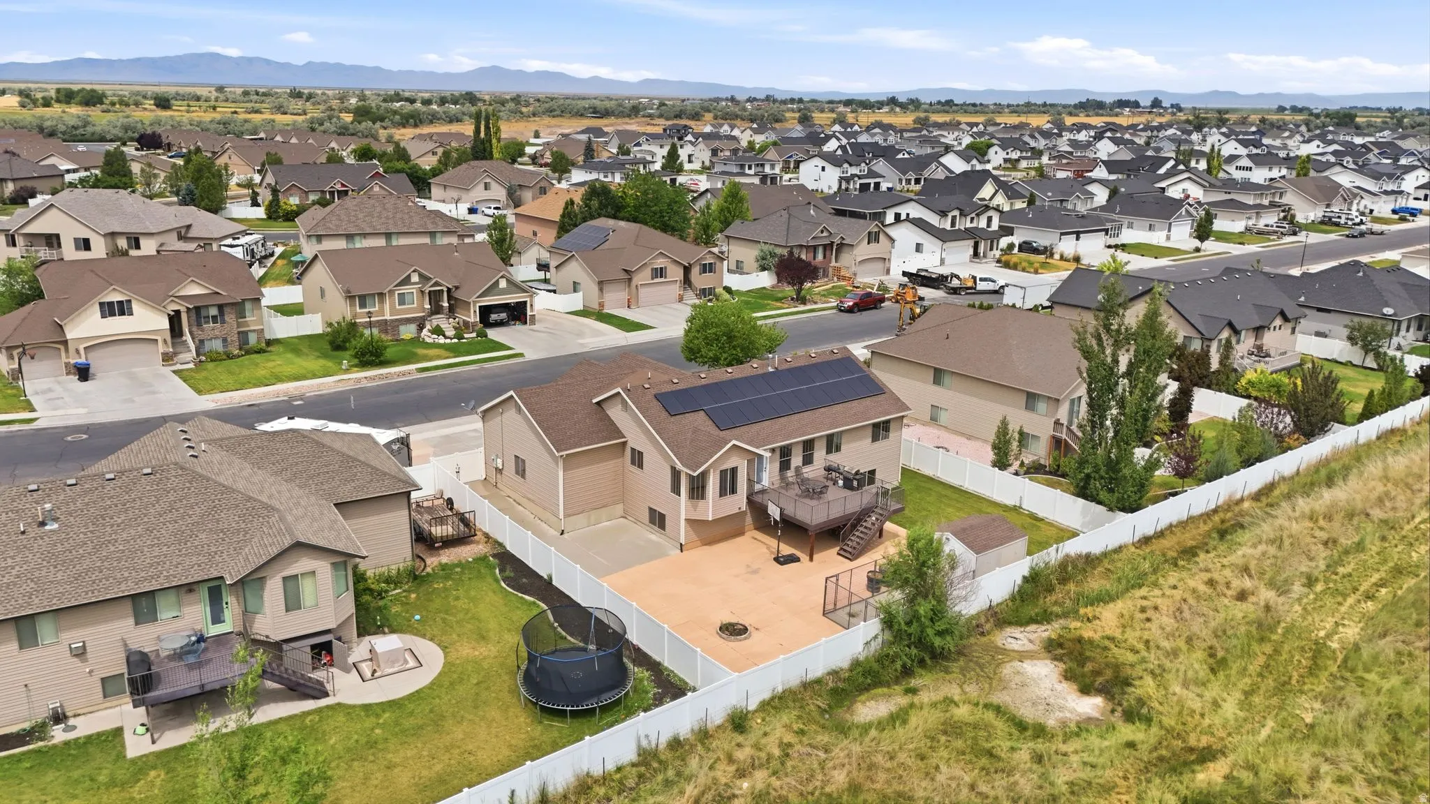 Aerial view of a residential neighborhood featuring a property with a multi-level deck, ground-level patio, and solar panels on the roof