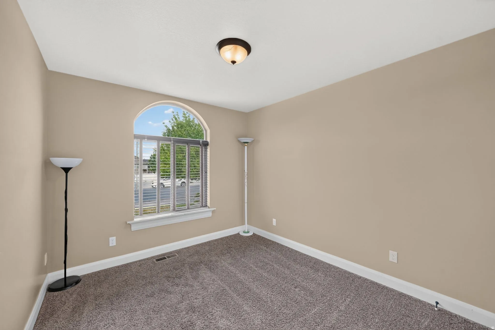 Room featuring an arched window with horizontal blinds, neutral wall paint, and textured carpeting