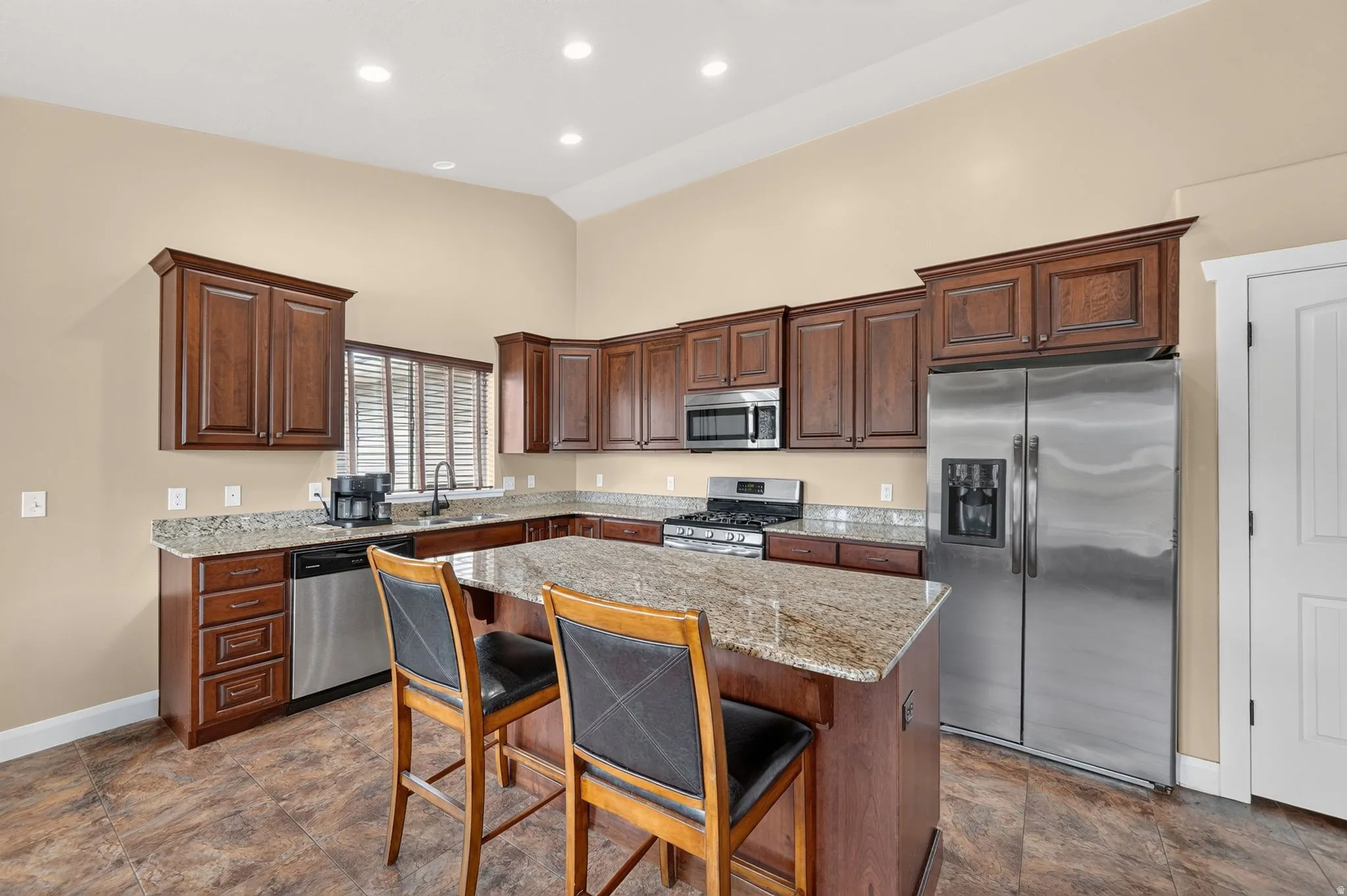 Kitchen featuring an L-shaped layout with dark wood cabinetry, granite countertops, and stainless steel appliances